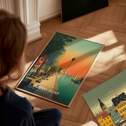 A child sits on a wooden floor, gazing at a vibrant poster featuring Düsseldorfs skyline, with a river, trees, and the iconic television tower under a colorful sunset. The poster is framed.