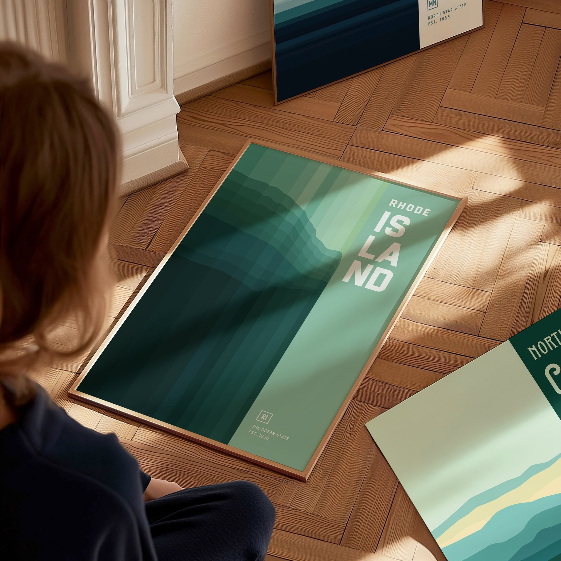 A person observes a Rhode Island poster with abstract green and blue hues on a wooden floor. The design features bold text, creating a modern aesthetic.