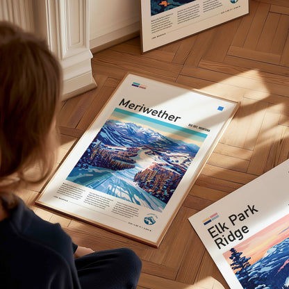 A person sits on a wooden floor, viewing a framed Meriwether ski run poster featuring snowy mountains and trees. Another poster titled Elk Park Ridge is partially visible.