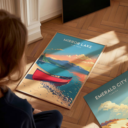 A child is sitting on a wooden floor, gazing at a colorful poster featuring Mirror Lake, New York. The artwork depicts a serene lake scene with a red canoe, vibrant mountains, and a sunset sky, capturing the tranquil beauty of.