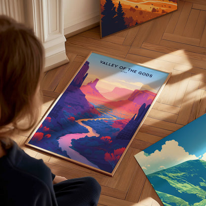 A person sits on a wooden floor, admiring a colorful Valley of the Gods poster depicting a vibrant desert landscape with winding river and rock formations.