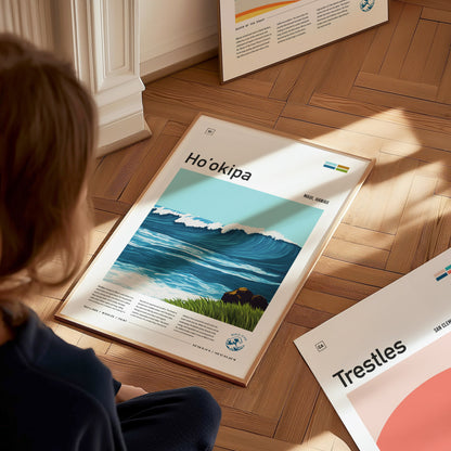 A person gazes at a framed poster of Hookipa Beach featuring a vibrant wave illustration, placed on a wooden floor alongside other framed artworks.