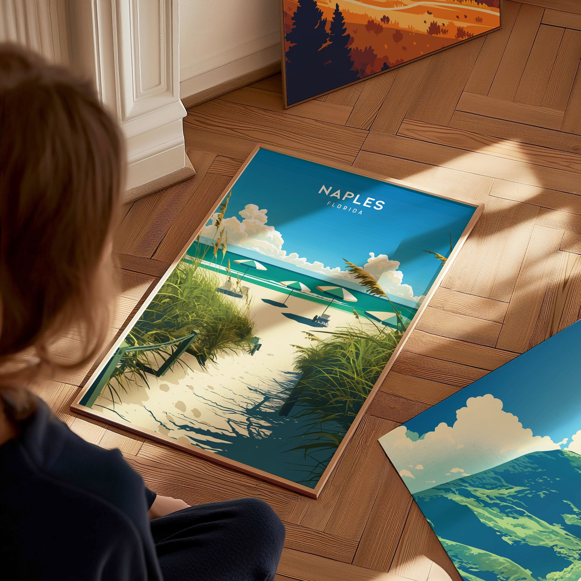 A person looks at a Naples, Florida poster featuring a beach path lined with grass leading to the ocean, under a blue sky with clouds.