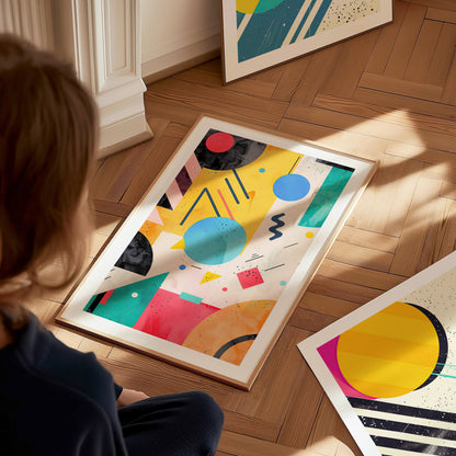 A person sits on a wooden floor, observing a vibrant abstract poster featuring bold geometric shapes and vivid colors, with two similar posters nearby.