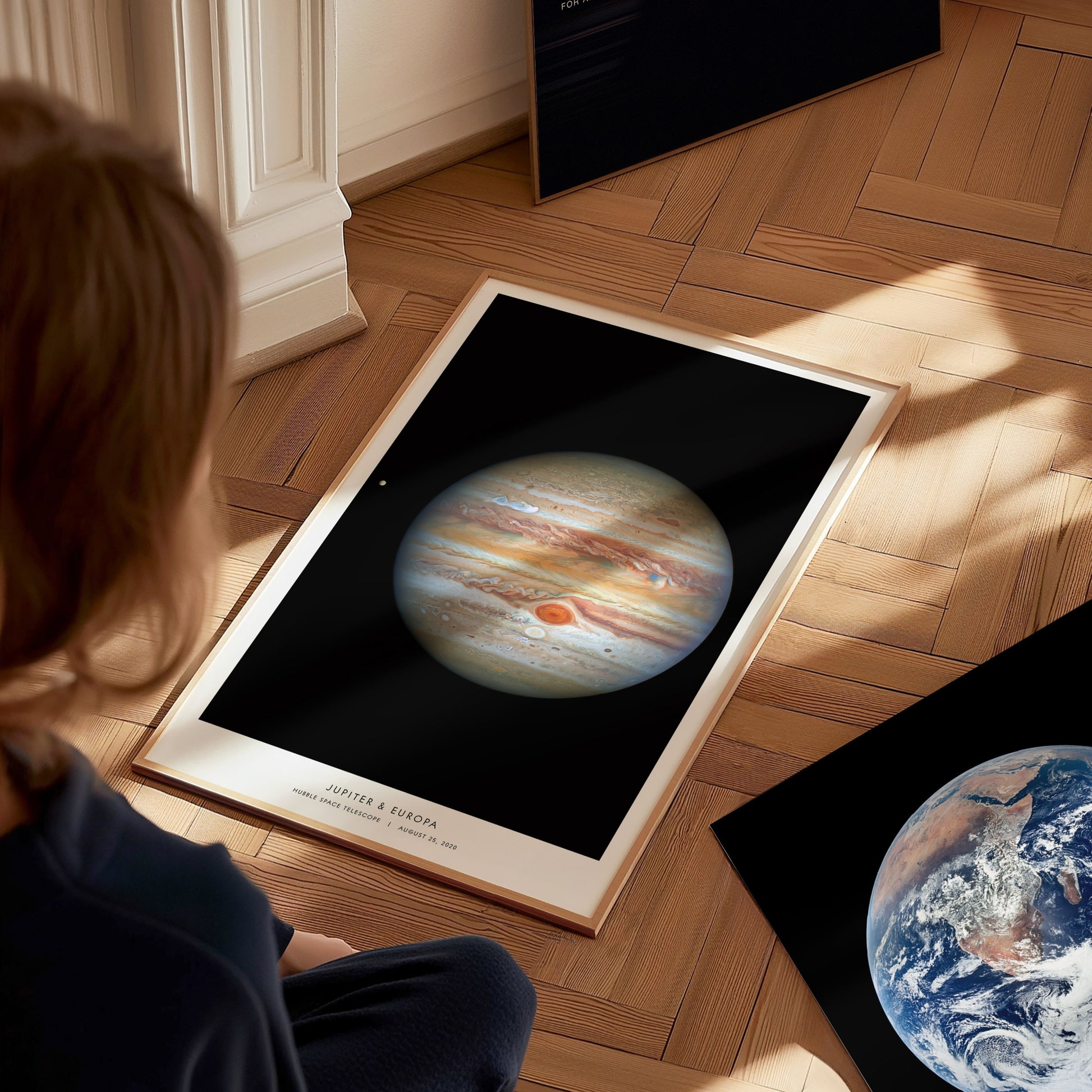 Person looking at a framed poster of Jupiter on a wooden floor.