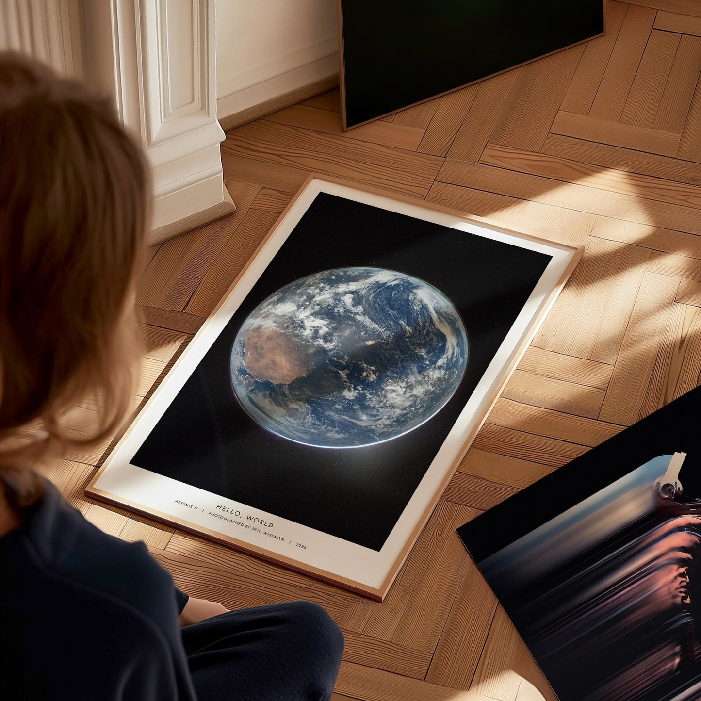 A child sits on a wooden floor, gazing at a framed poster featuring a stunning view of Earth from space, with vibrant colors highlighting the planets surface.