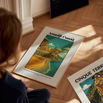 Person looking at a framed poster of the Amalfi Coast on a wooden floor.