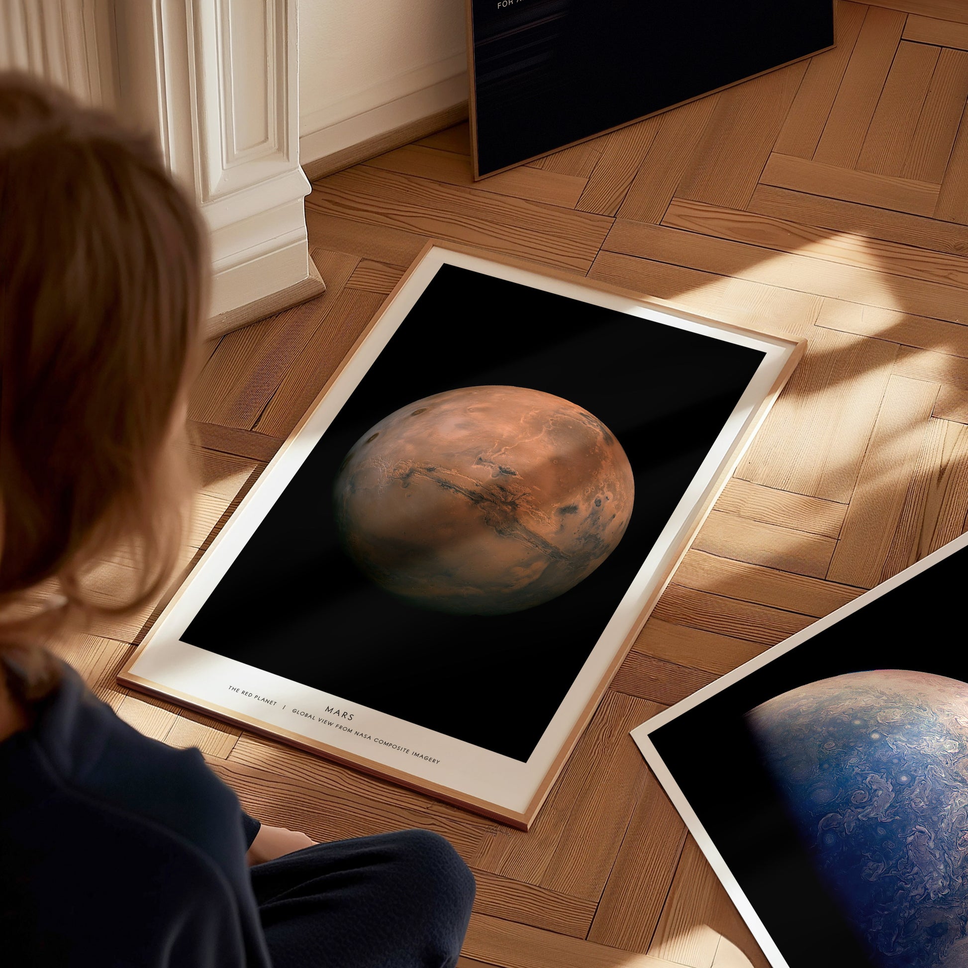 Person looking at a framed poster of Mars on a wooden floor
