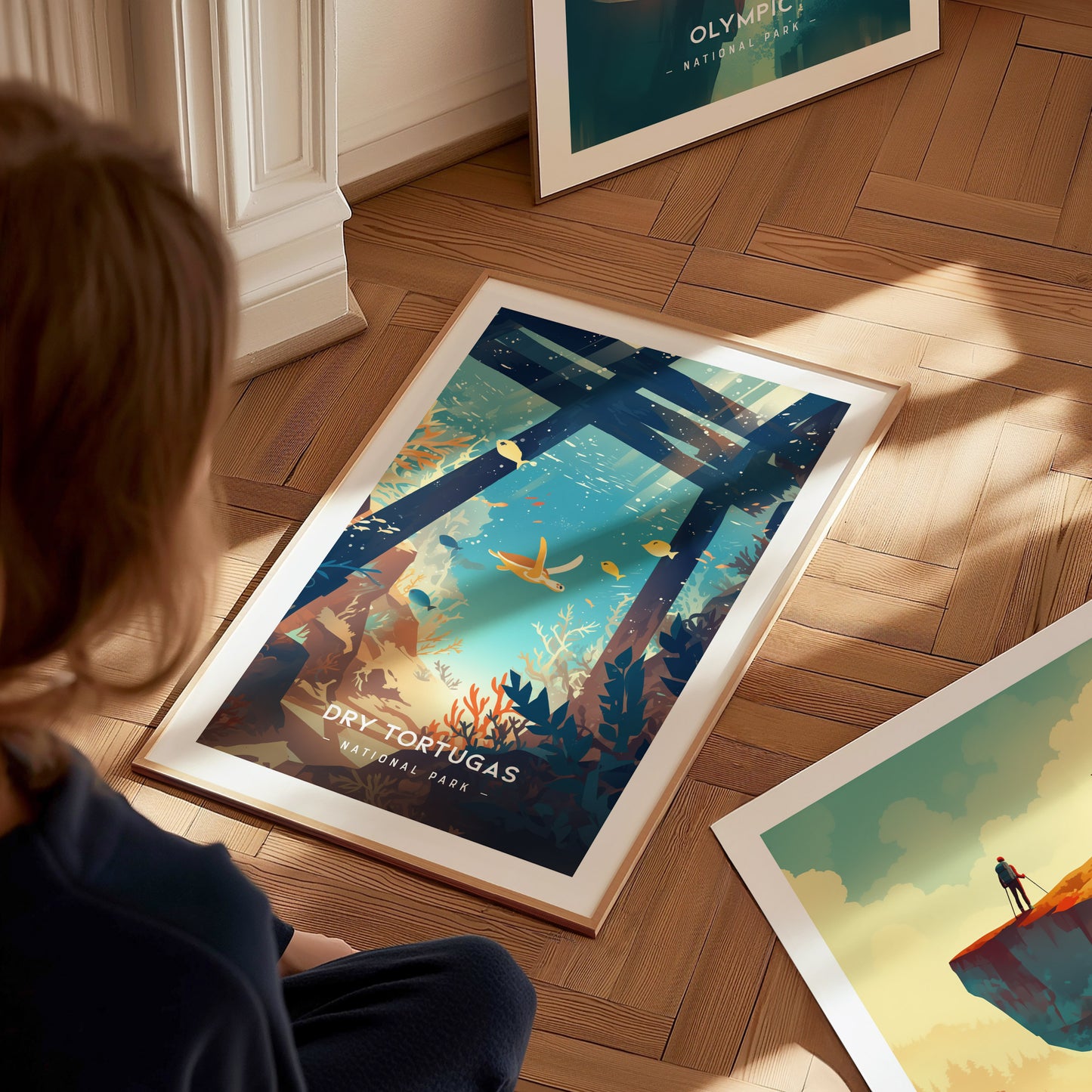 A person sits on a wooden floor, observing a framed poster of Dry Tortugas National Park featuring an underwater scene with coral and fish, illuminated by sunlight.