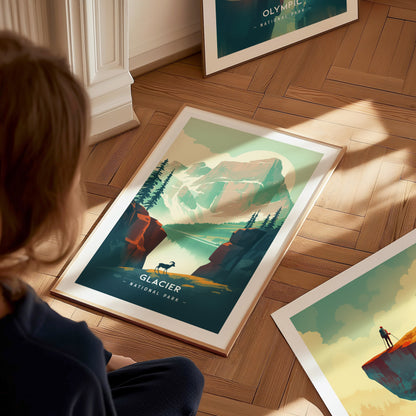 A person views a framed Glacier National Park poster on a wooden floor, depicting mountains, trees, and a bighorn sheep. Another poster is partially visible nearby.