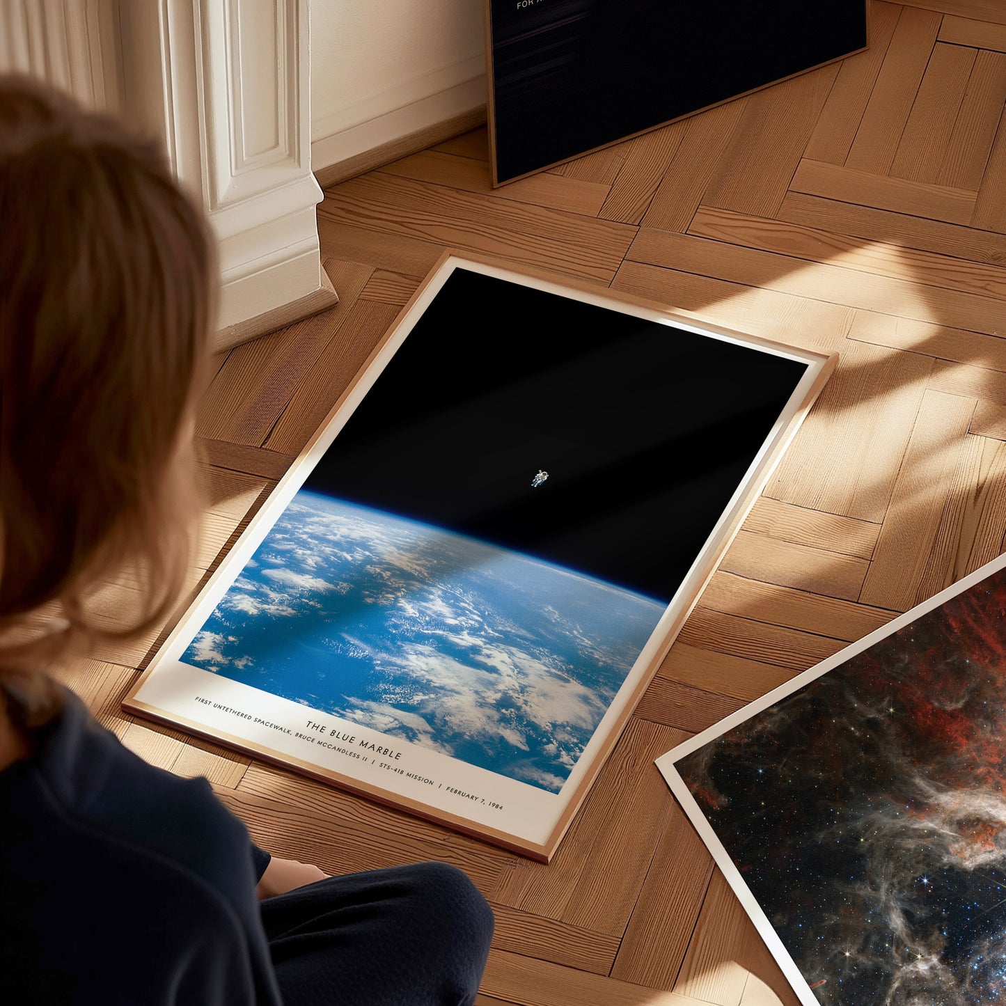 Person looking at a framed photograph of Earth from space on a wooden floor.