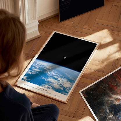Person looking at a framed photograph of Earth from space on a wooden floor.