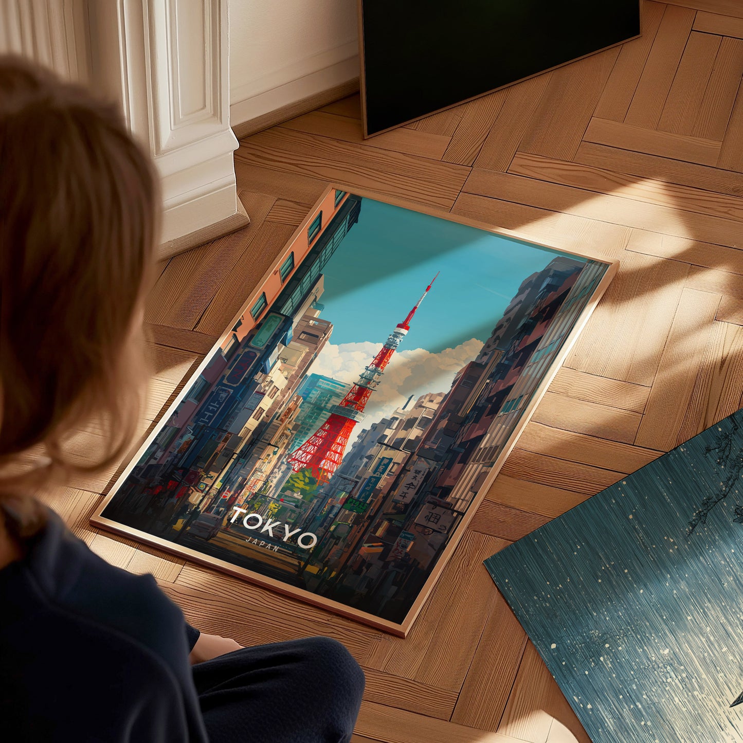 A person looks at a vibrant Tokyo Tower poster on a wooden floor. The poster depicts the tower amidst a cityscape under a clear blue sky.
