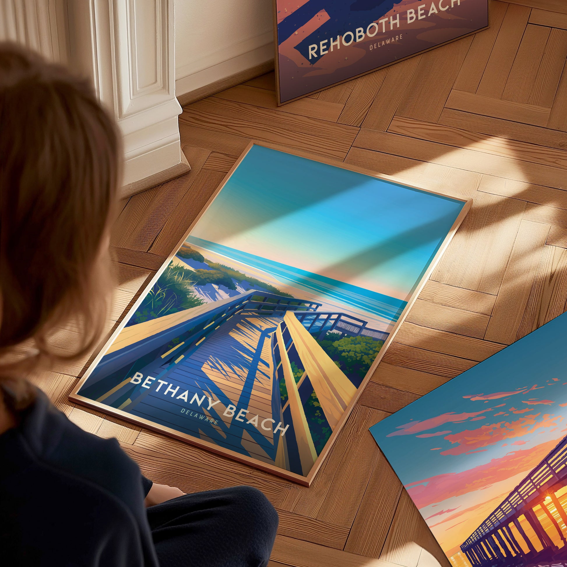 A person sits on a wooden floor, looking at a vibrant Bethany Beach poster depicting a boardwalk leading to the ocean under a clear sky.