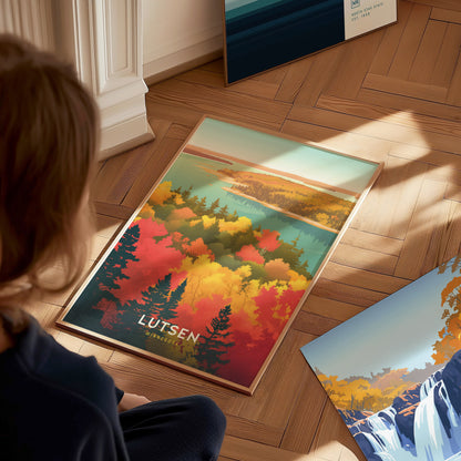 A person views a colorful poster featuring autumn foliage with vibrant red, orange, and yellow trees, a blue lake, and the text Lutsen Minnesota on a wooden floor.