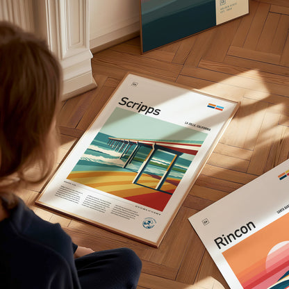 A person looks at a colorful poster of Scripps Pier on a wooden floor. The poster features bold lines and vibrant colors depicting the pier and ocean waves.
