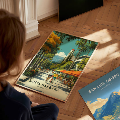 Person looking at a 'Santa Barbara, California' travel poster on a wooden floor.