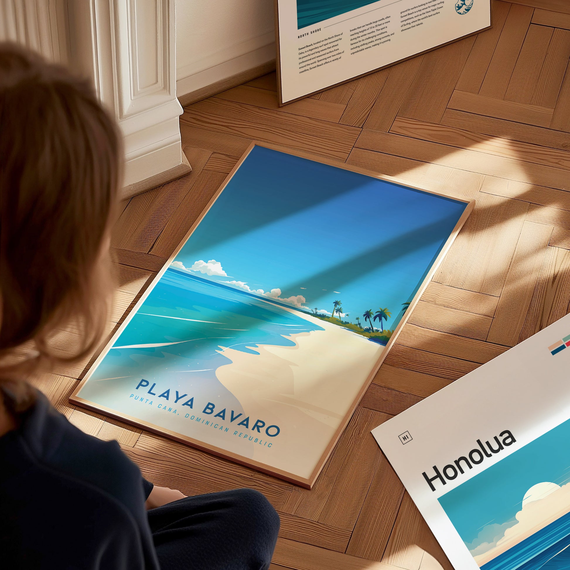 A person sits on a wooden floor, looking at a vibrant art print featuring a beach scene of Playa Bavaro in the Dominican Republic. The poster showcases a clear blue sky, soft white sand, and palm trees, evoking a tropical paradise feel.