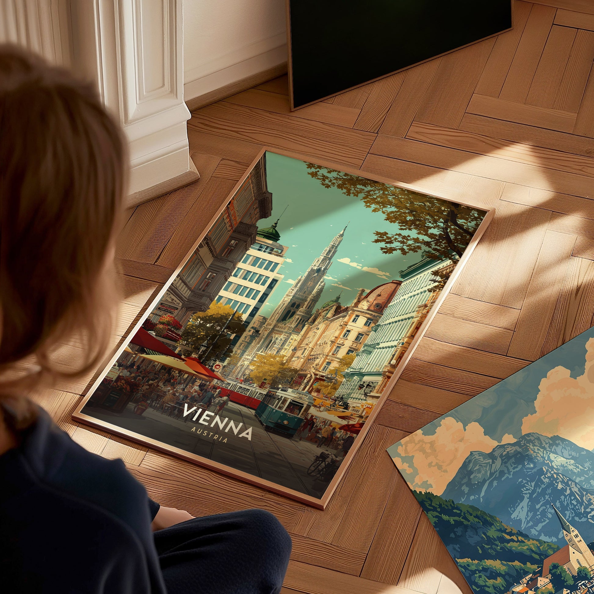 A child sits on a wooden floor, gazing at a vibrant poster of Vienna, Austria, featuring a bustling city scene with historic architecture and trees. Nearby, a second poster showcases a picturesque mountain landscape.