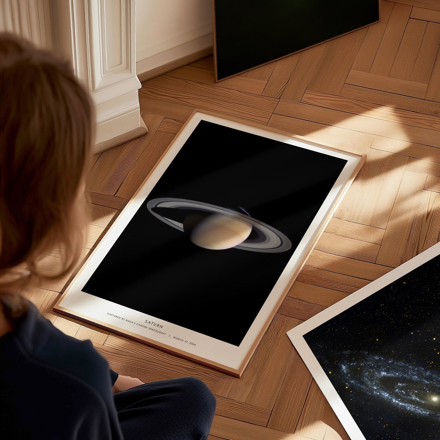 Person looking at a framed poster of Saturn on a wooden floor
