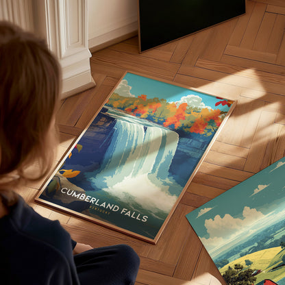 A child sits on a wooden floor, gazing at a colorful poster of Cumberland Falls, featuring a majestic waterfall surrounded by vibrant autumn foliage.
