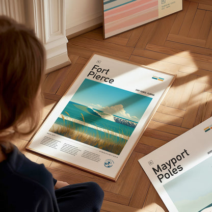 A person sits on a wooden floor gazing at a Fort Pierce poster featuring a coastal scene with waves and clouds. Additional posters are partially visible nearby.
