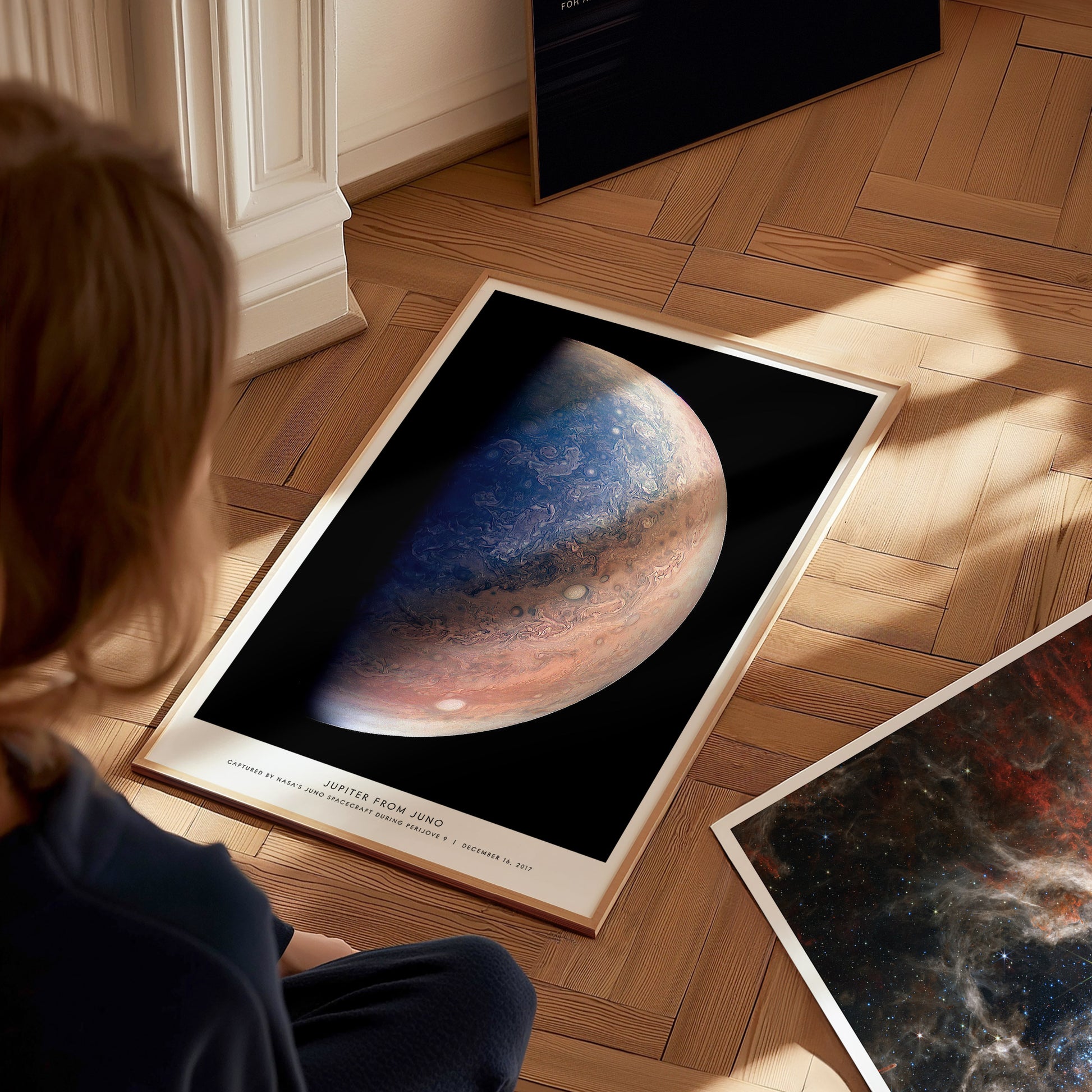 Person looking at a framed poster of Jupiter on a wooden floor