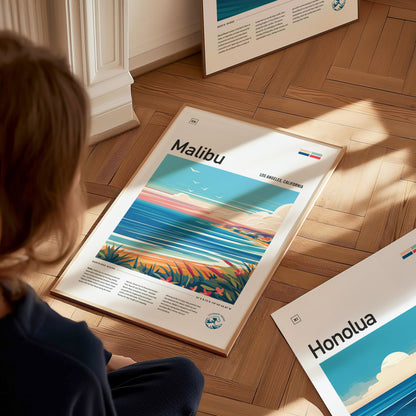 A person looks at a framed poster on the floor titled Malibu, featuring an abstract coastline with vibrant colors and a clear sky.