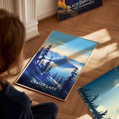 A person looks at a Crater Lake National Park poster on a wooden floor, depicting serene blue waters and tall trees under a clear sky.