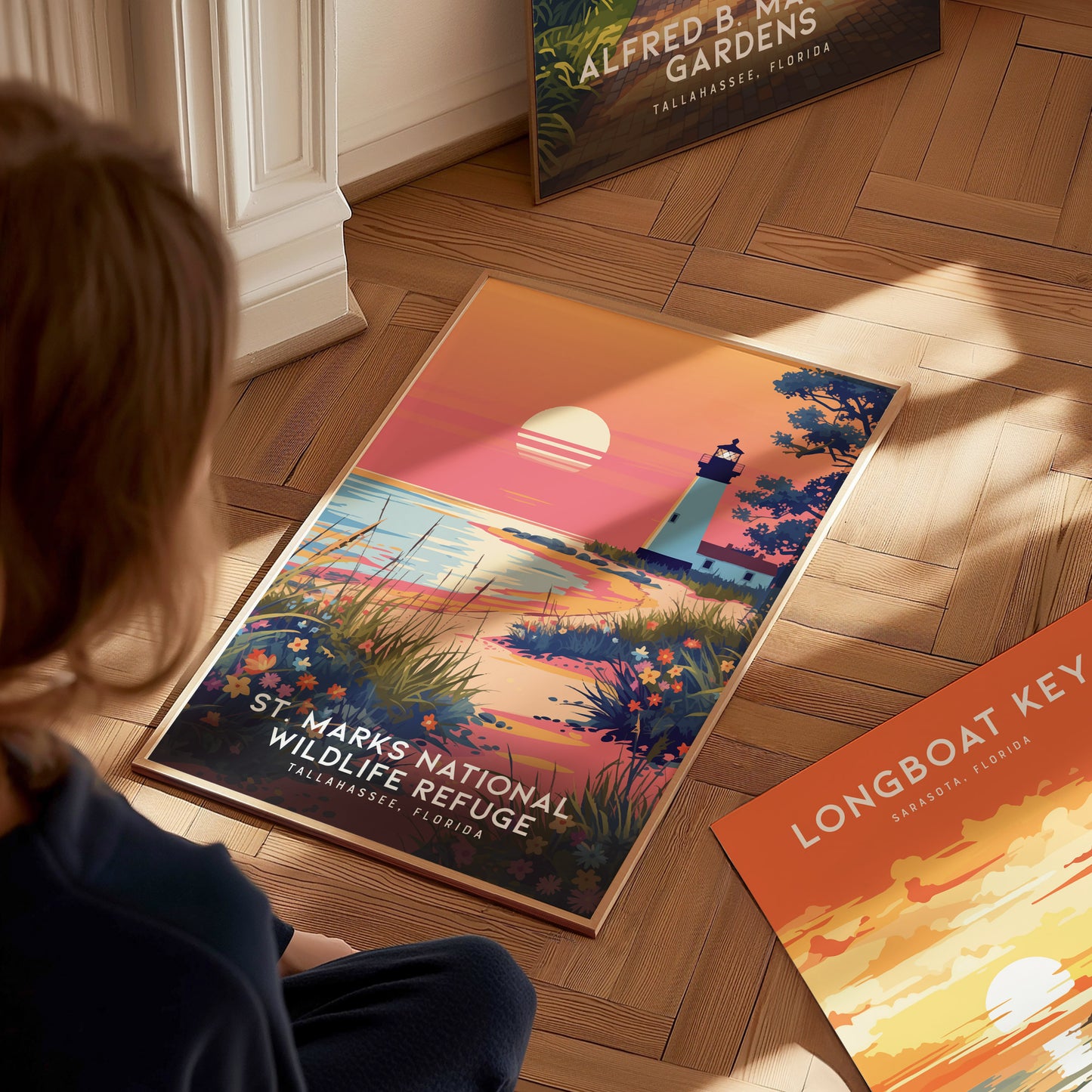 A person looks at a St. Marks National Wildlife Refuge poster featuring a lighthouse at sunset with wildflowers and marshes. Additional posters are partially visible on the wooden floor.
