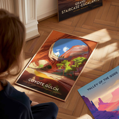 A person looks at a colorful poster of Coyote Gulch, depicting vibrant canyon walls and trees, placed on a wooden floor. Nearby, other posters are partially visible.