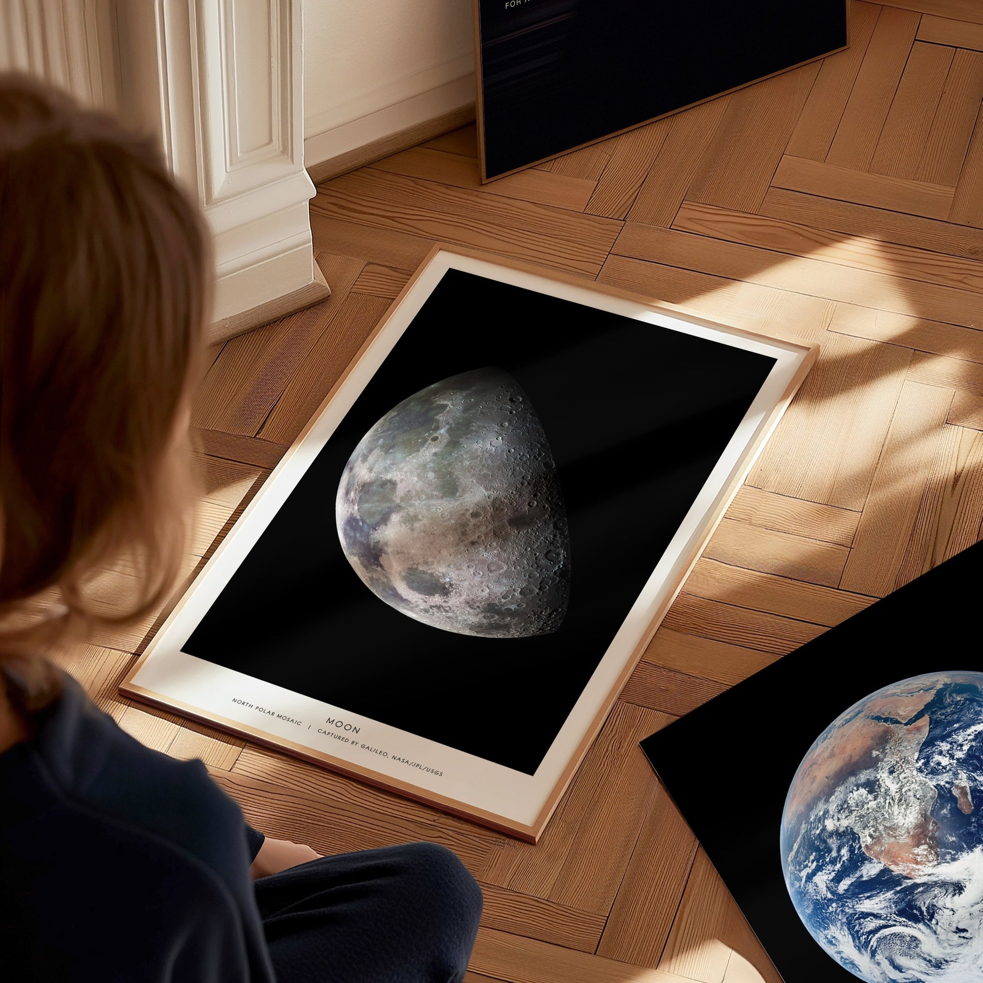 Person looking at a framed image of the moon on a wooden floor.