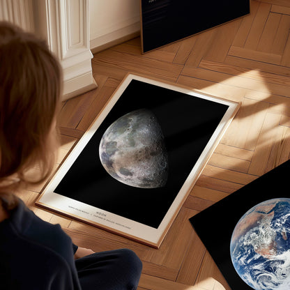 Person looking at a framed image of the moon on a wooden floor.