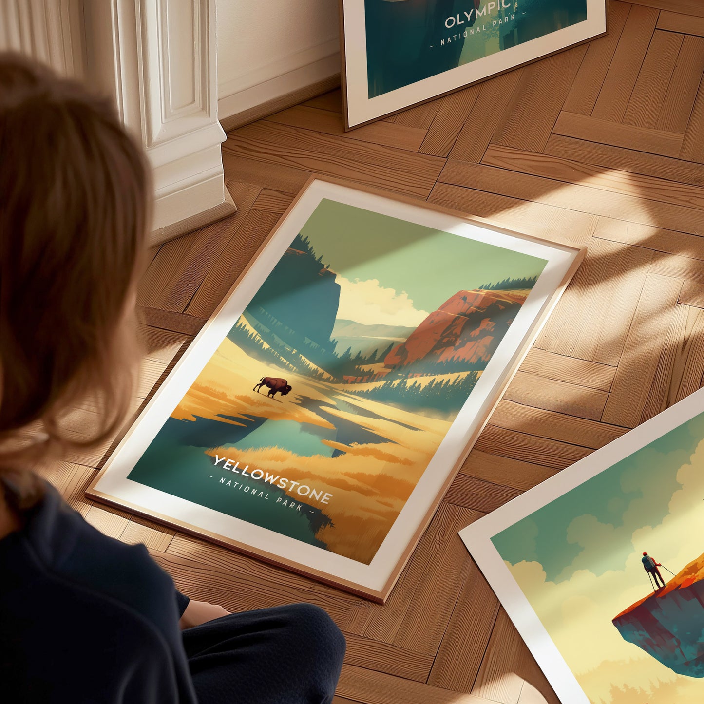 A person sits on a wooden floor, viewing a framed Yellowstone National Park poster featuring a stylized landscape with a buffalo and colorful mountains.