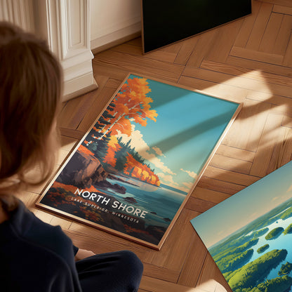 A child sits on a wooden floor, gazing at a colorful poster featuring the North Shore of Lake Superior.