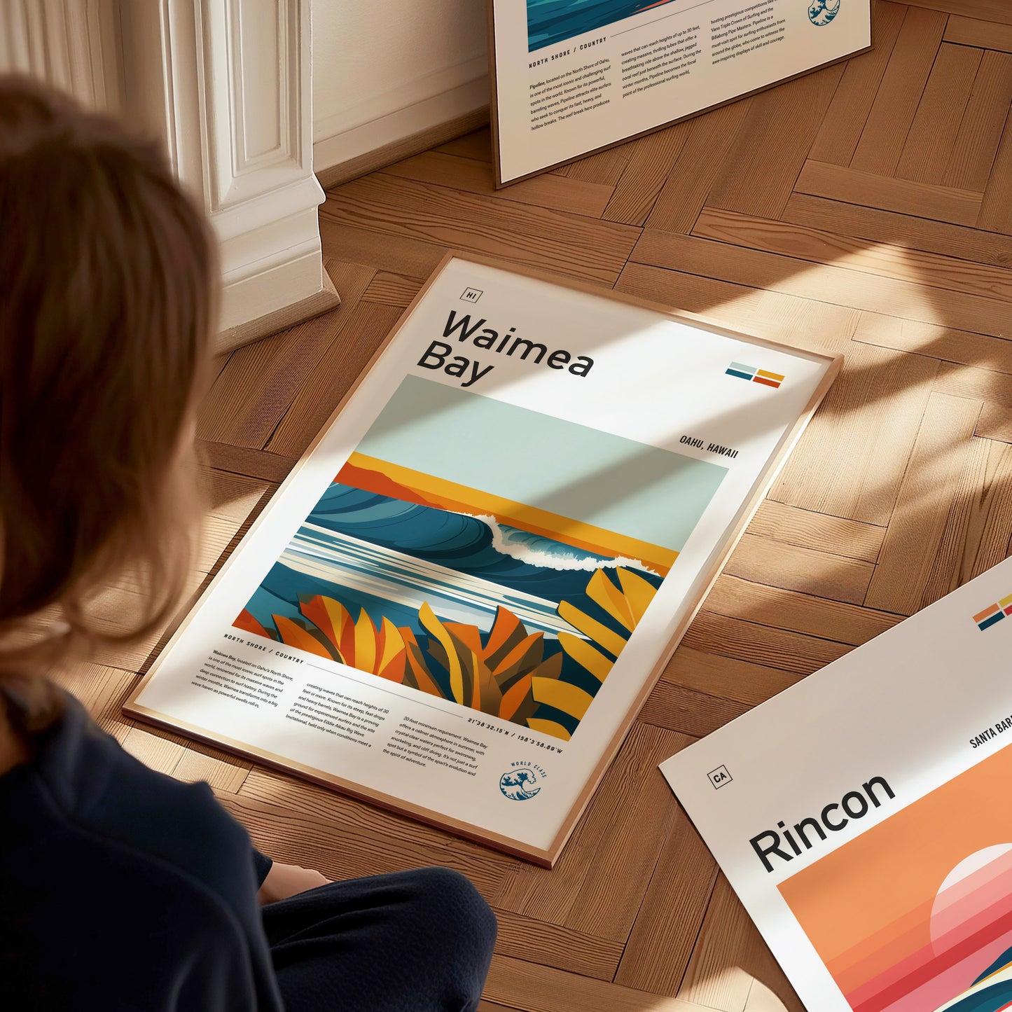 A person sits on a wooden floor, looking at a colorful Waimea Bay poster featuring waves and tropical foliage. Other posters are partially visible around them.