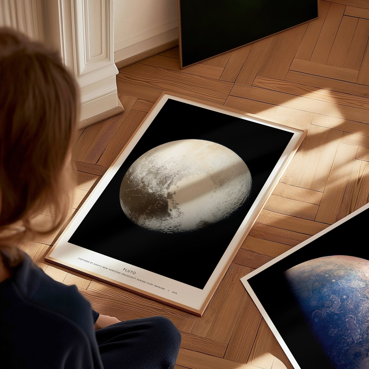 Person looking at a framed picture of Pluto and Jupiter on a wooden floor.