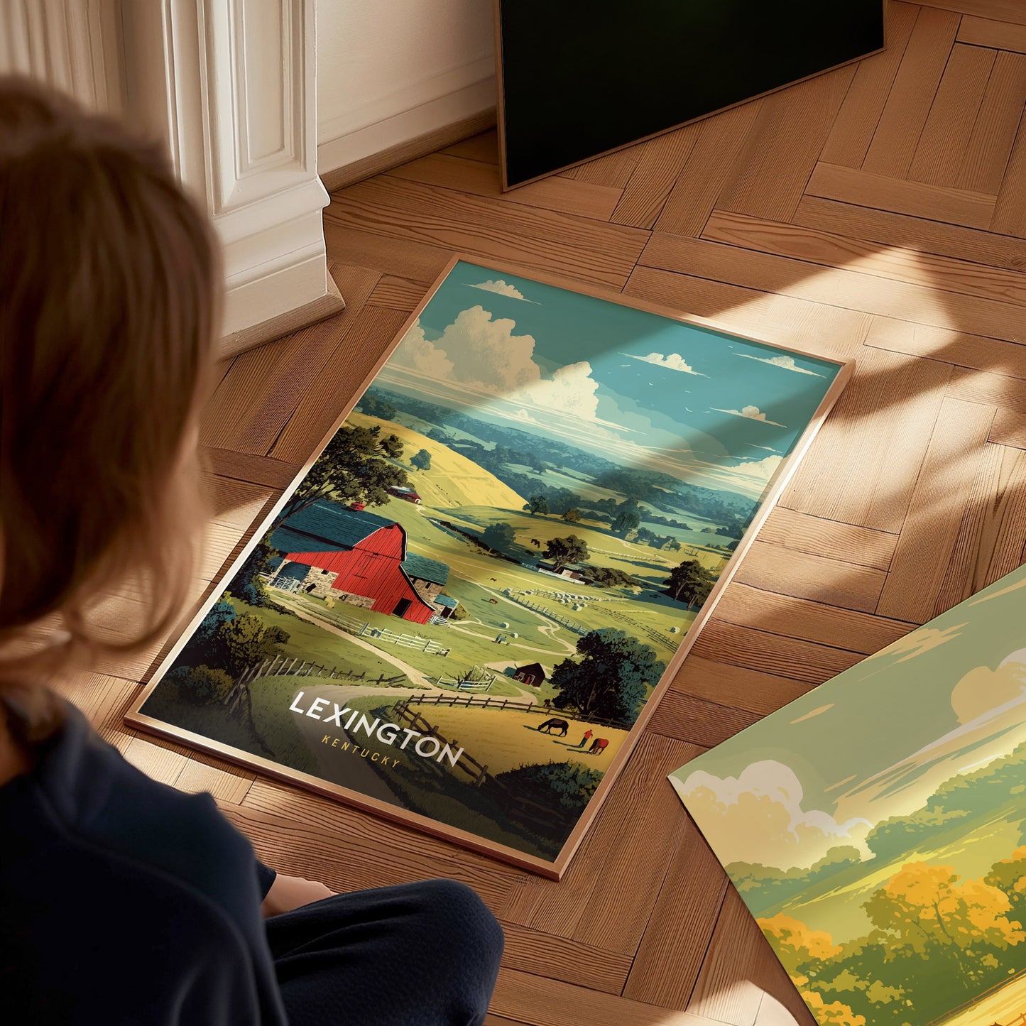 A child sits on a wooden floor, gazing at a colorful poster featuring a scenic landscape of rolling green hills and a red barn. The poster depicts the text LEXINGTON at the top, surrounded by fluffy clouds and a serene countryside setting.