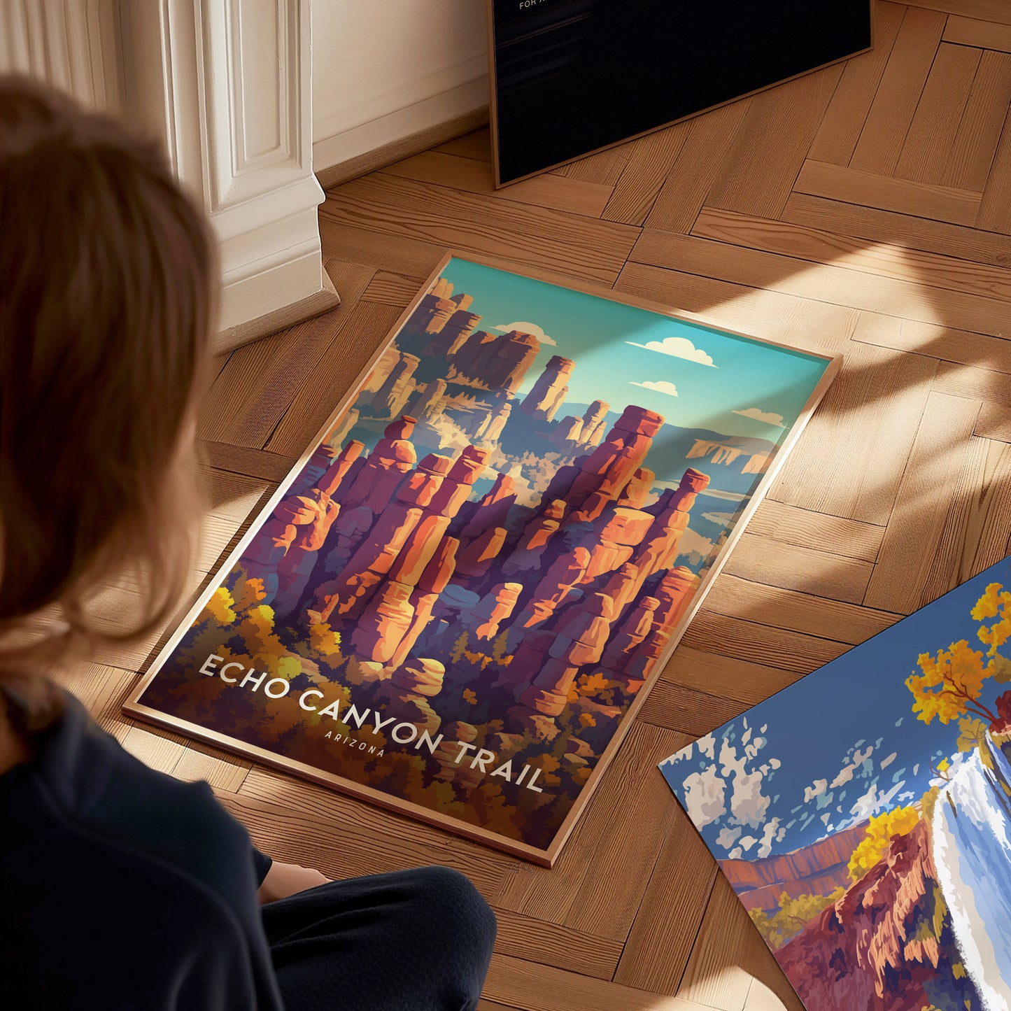 A young child sits on a wooden floor, intently observing a colorful poster featuring the Echo Canyon Trail, showcasing vibrant red rock formations and a blue sky.