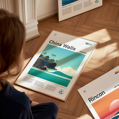 A person sits on a wooden floor, looking at a framed China Walls poster featuring a coastal scene with turquoise waves, cliffs, and palm trees. Additional posters are partially visible.