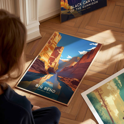 A person looks at a colorful Big Bend National Park poster on a wooden floor, depicting a river and canyon landscape under a blue sky with clouds.