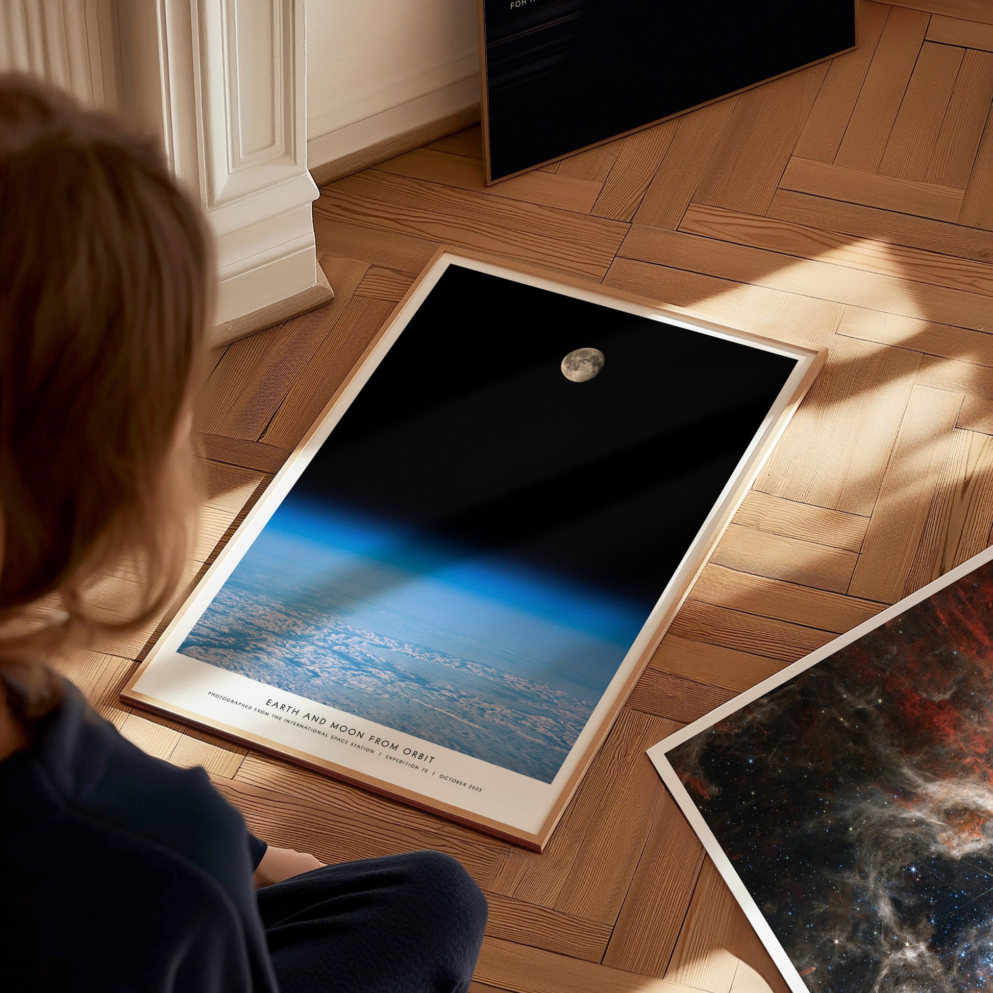 Person sitting on the floor looking at framed space posters with Earth and moon views.