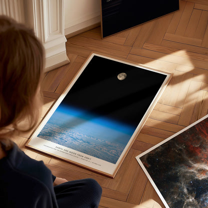 Person sitting on the floor looking at framed space posters with Earth and moon views.
