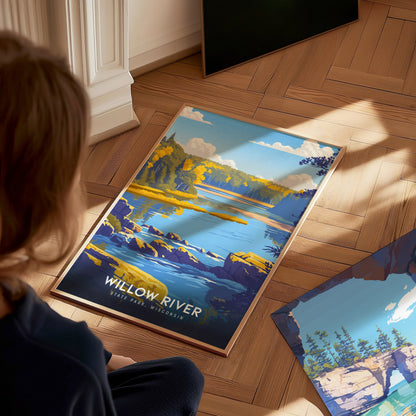 A child sits on a wooden floor, gazing at a vibrant travel print featuring Willow River State Park in Wisconsin.