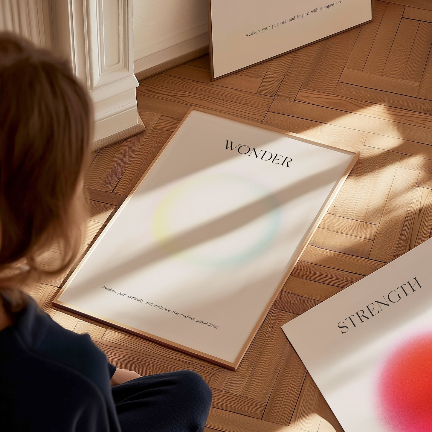 A child sits on a wooden floor, gazing at a framed art print that features the word WONDER alongside a soft, colorful gradient.