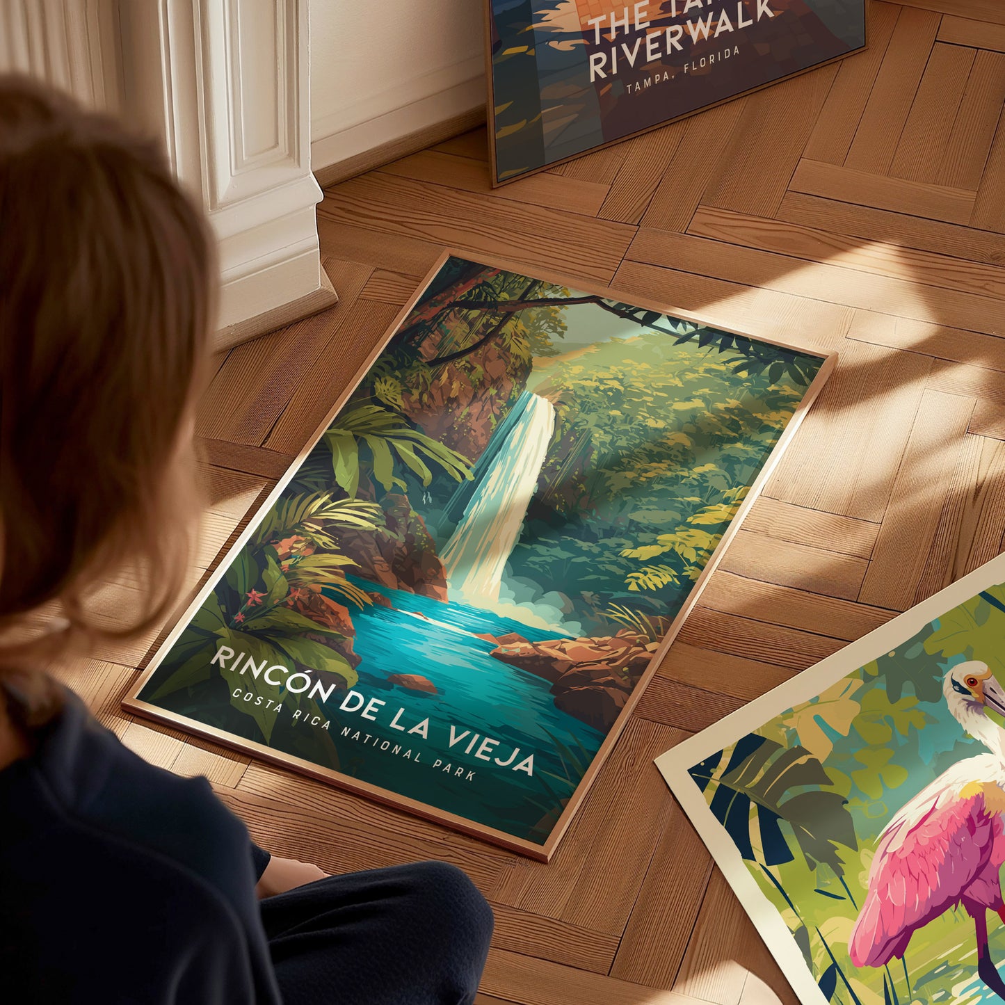 A child is seated on a wooden floor, gazing at a vibrant poster featuring a waterfall surrounded by lush greenery, labeled Rincón de la Vieja, Costa Rica National Park.