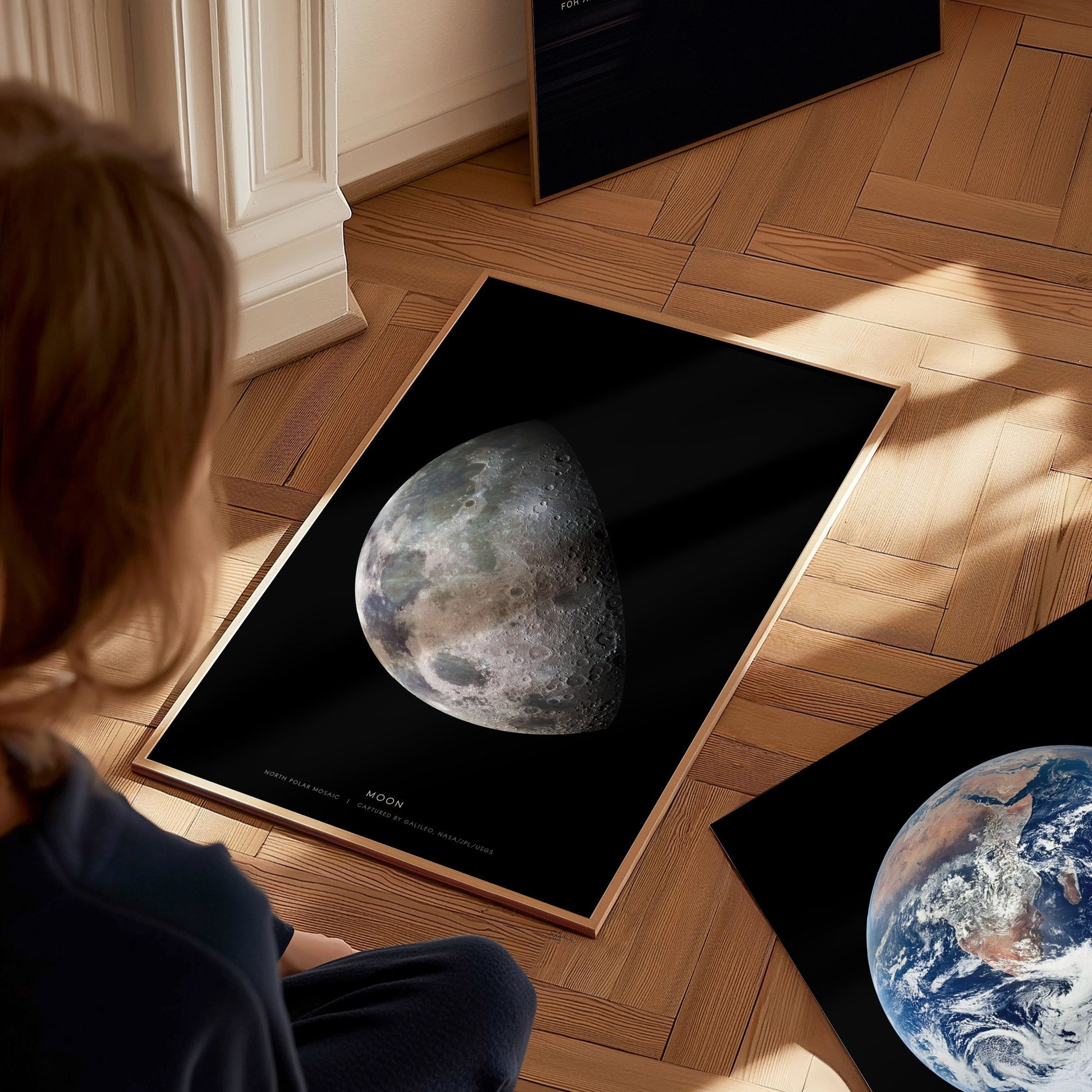 Person looking at a framed poster of the moon on a wooden floor.