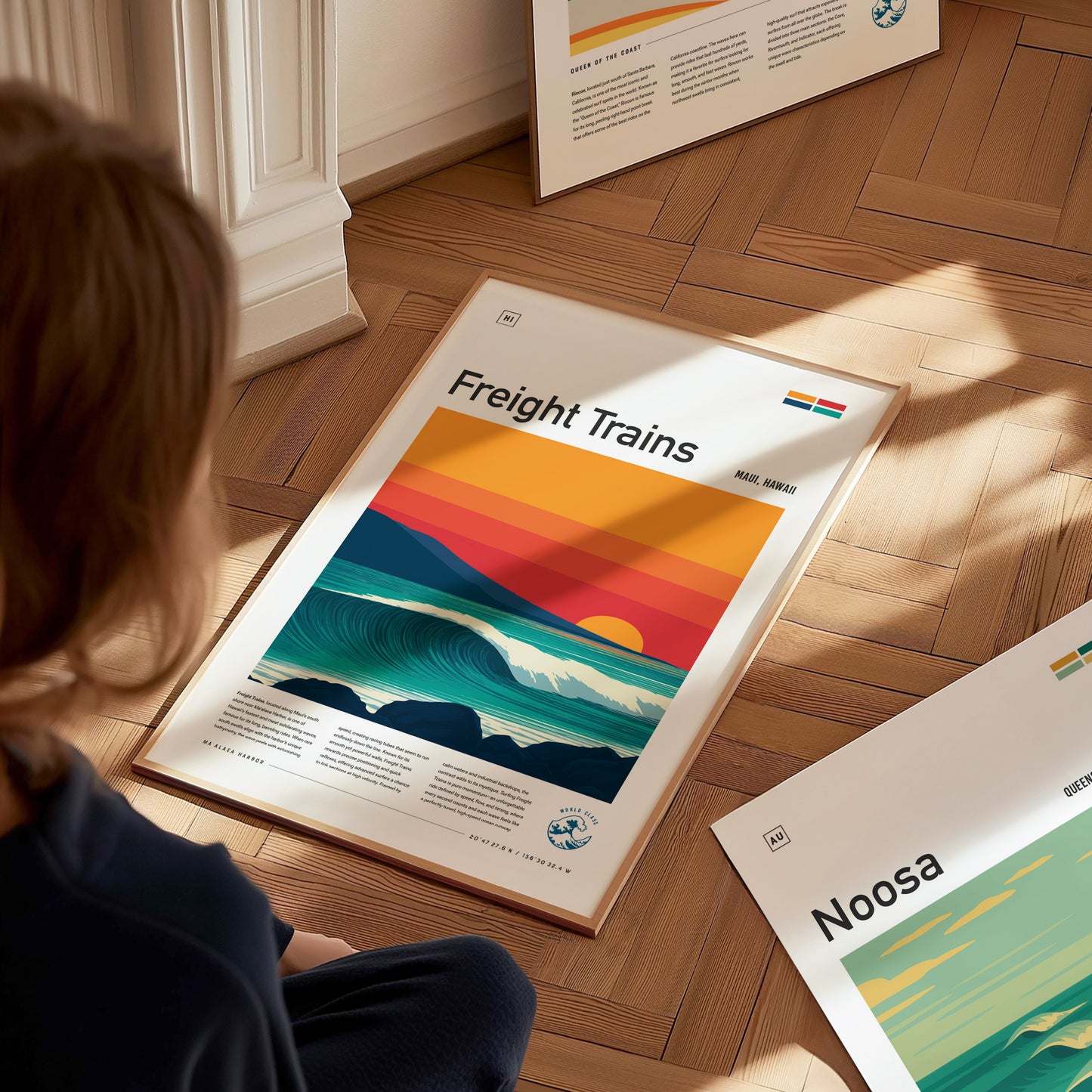 A child sits on a wooden floor, gazing at a colorful poster titled Freight Trains, featuring stylized waves and a sunset in vibrant hues of orange, red, and blue.