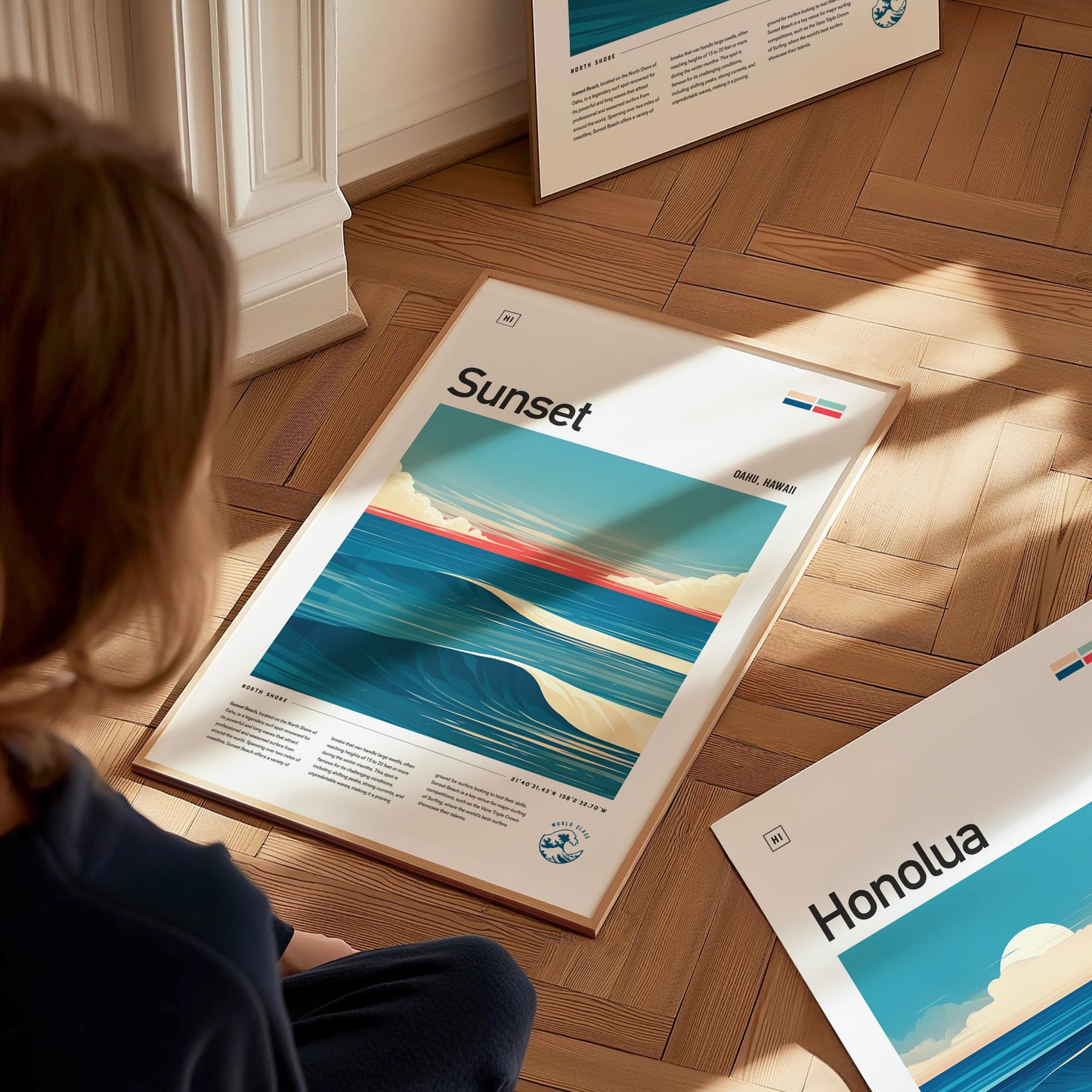 A person sits on a wooden floor, looking at colorful surf art posters. The poster in focus features ocean waves under a vibrant sky with the word Sunset prominently displayed.