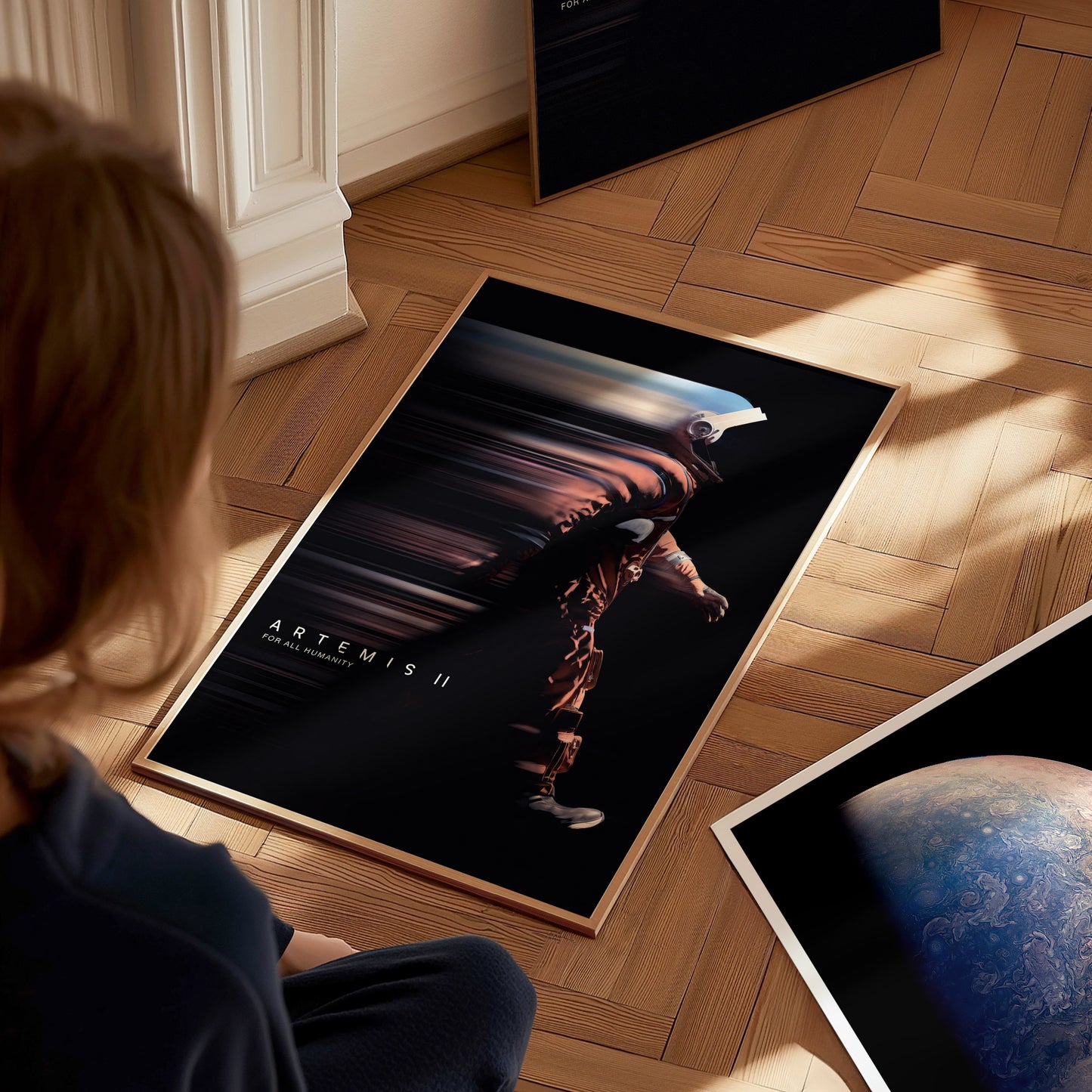 Person sitting on the floor looking at a large Artemis II NASA poster on a wooden floor.